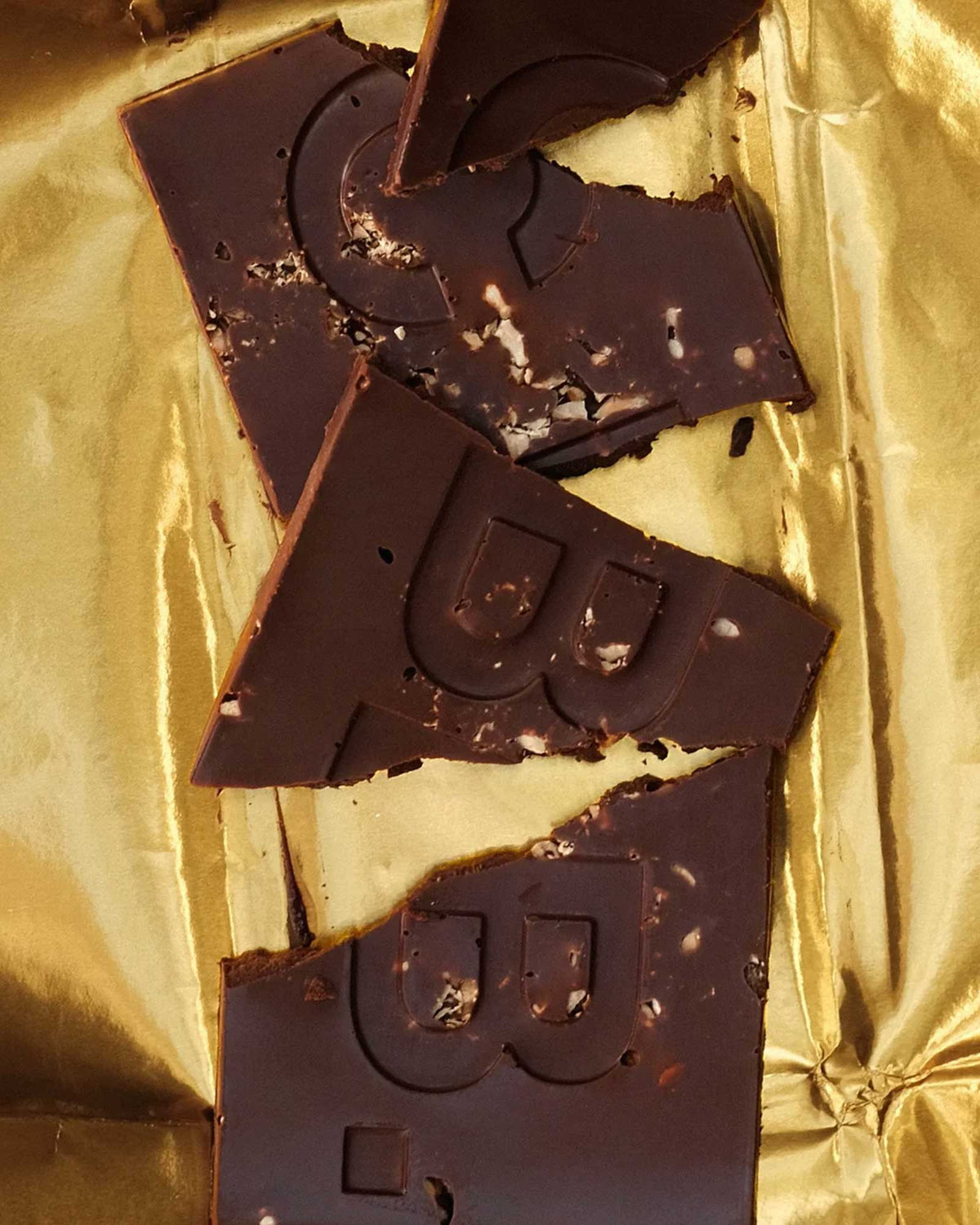 Broken pieces of a Casa Bosques dark chocolate bar sitting on a sheet on gold foil.
