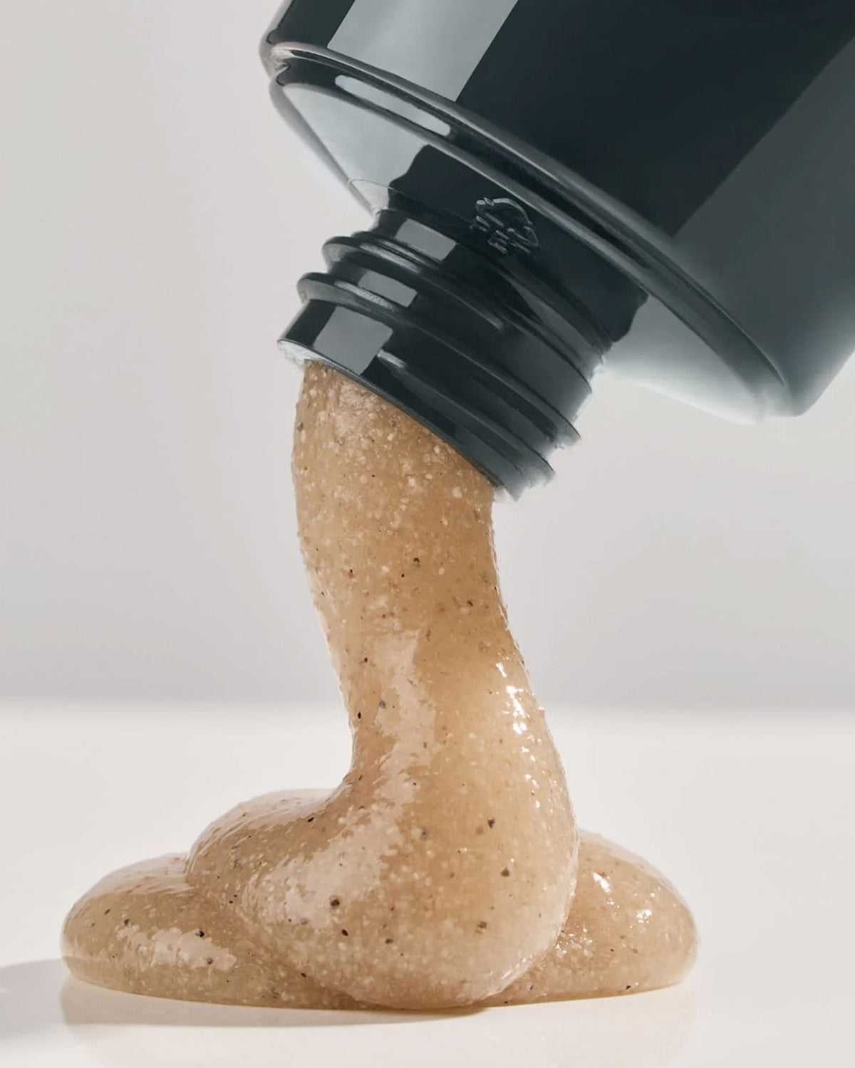 A squeeze tube of Leif Caviar Lime Body Scrub, a navy blue bottle with a light brown, semi-translucent, textured cream coming out of the nozzle.