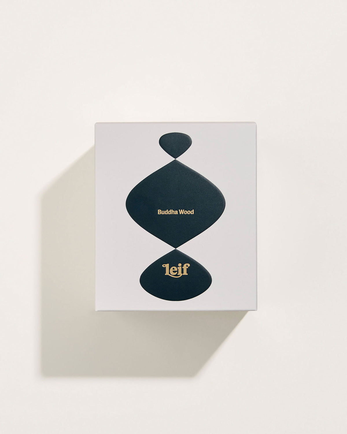 A square white box with a black abstract pattern with gold foil lettering which reads Buddha Wood Leif. Set on a white background.