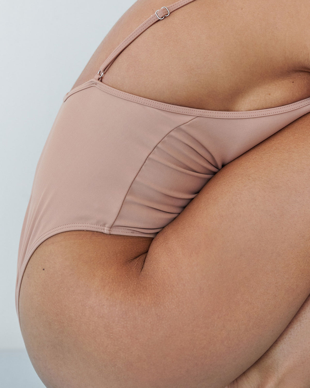 Close-up, side view of a woman in a one-piece nude-coloured bodysuit crouching down.