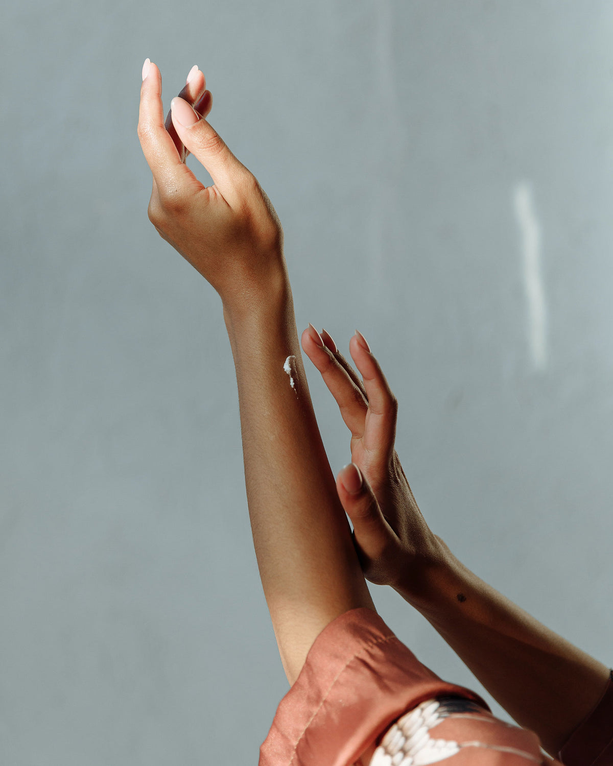 A woman applying a white cream to her arm against a light blue backdrop.