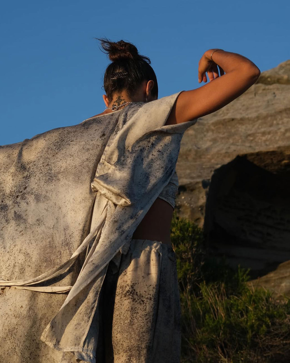 Woman dressed in purple and white coloured silk kimono robe and matching pants dances near large grey rock.