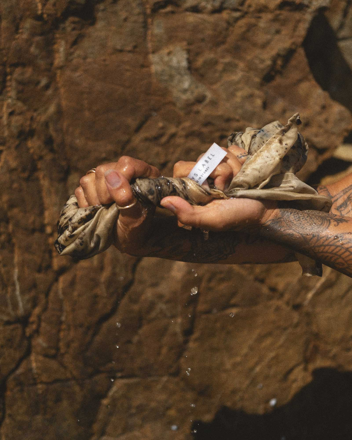 Two hands wringing water out of a light brown cloth against a brown rock.