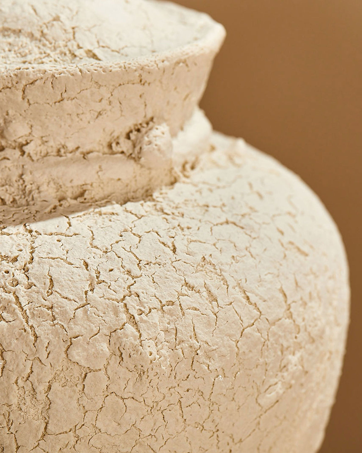 A close up of a heavily textured surface of a white, unglazed ceramic urn against an orange background.