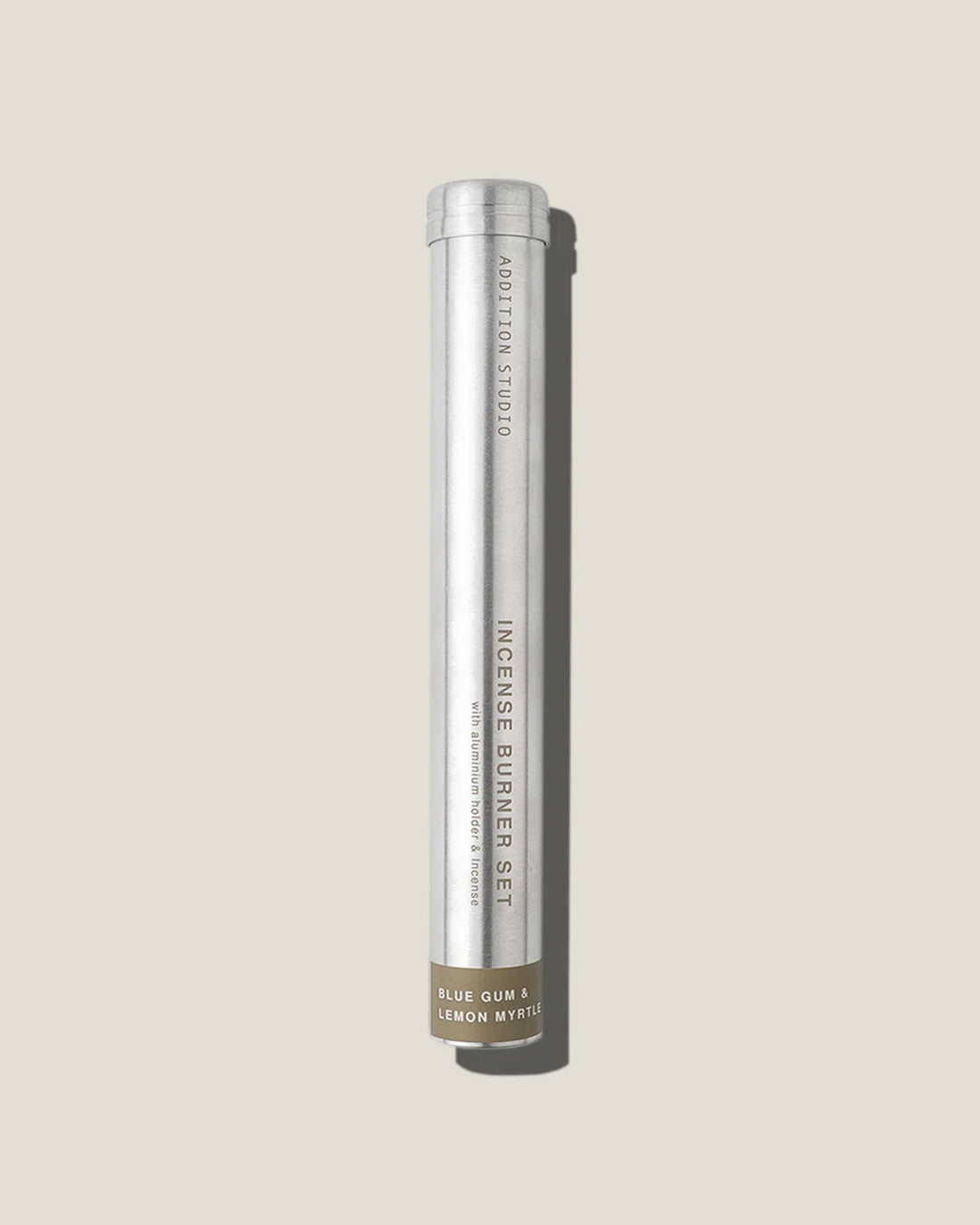A tall, slim aluminium canister with printed lettering reads Addition Studio Incense Burner Set, Blue gum and lemon myrtle on an off-white background.