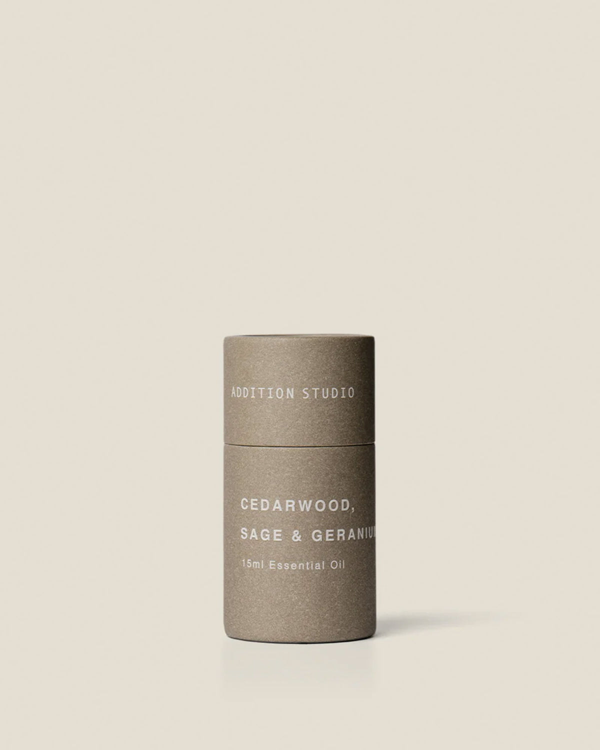 A small grey coloured cardboard canister with white printed text which reads Addition Studio Cedarwood, Sage and Geranium 15ml Essential Oil on an off-white background. 