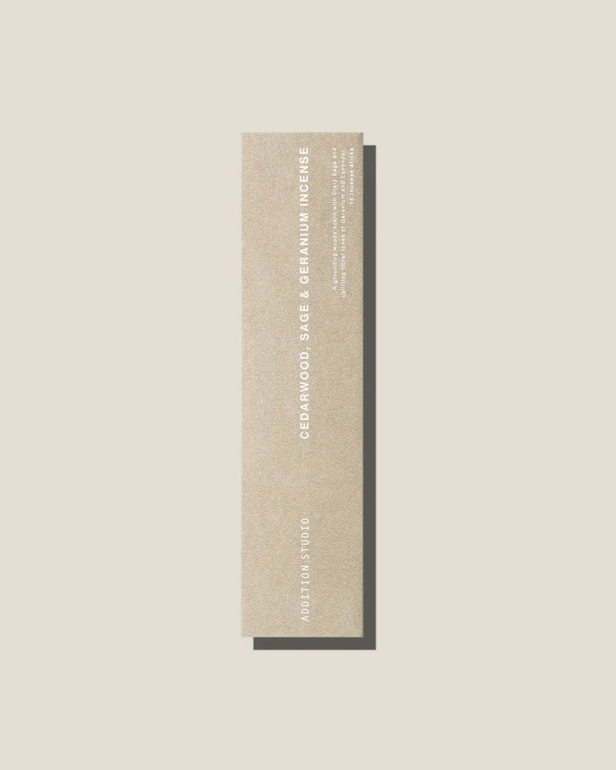 A stone coloured long, slim rectangular cardboard package with white type which reads Addition Studio CEDARWOOD, SAGE AND GERANIUM INCENSE, set on an off-white background.