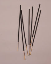 Seven black incense bamboo sticks laying on a dusty-pink background with light and shadow.