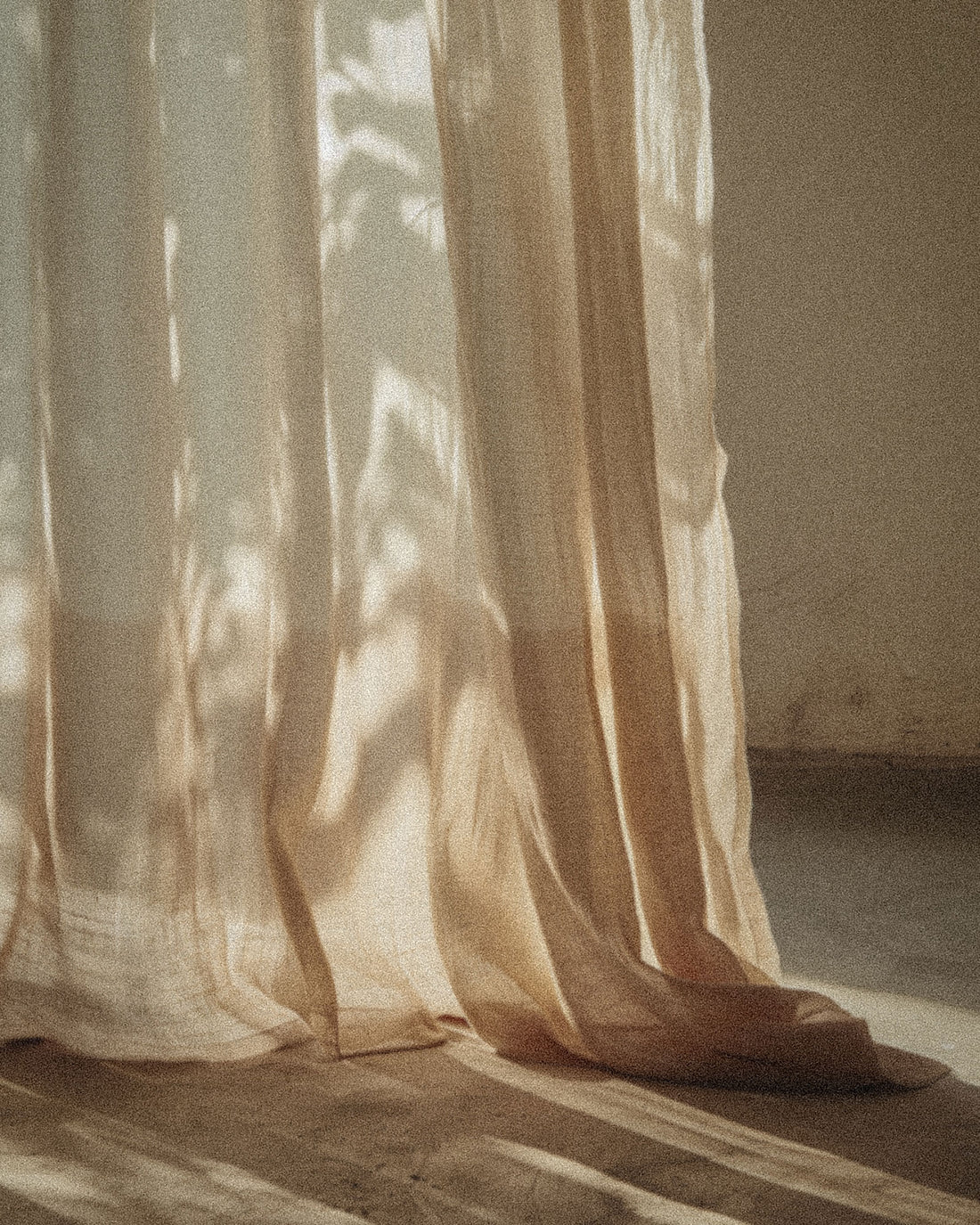 Sunlight filtering through a beige coloured curtain that is draped on the floor.