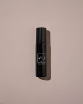 A black cylindrical roll-on bottle of AYU Rose Oil against a dusty pink background.