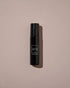 A black cylindrical roll-on bottle of AYU Rose Oil against a dusty pink background.