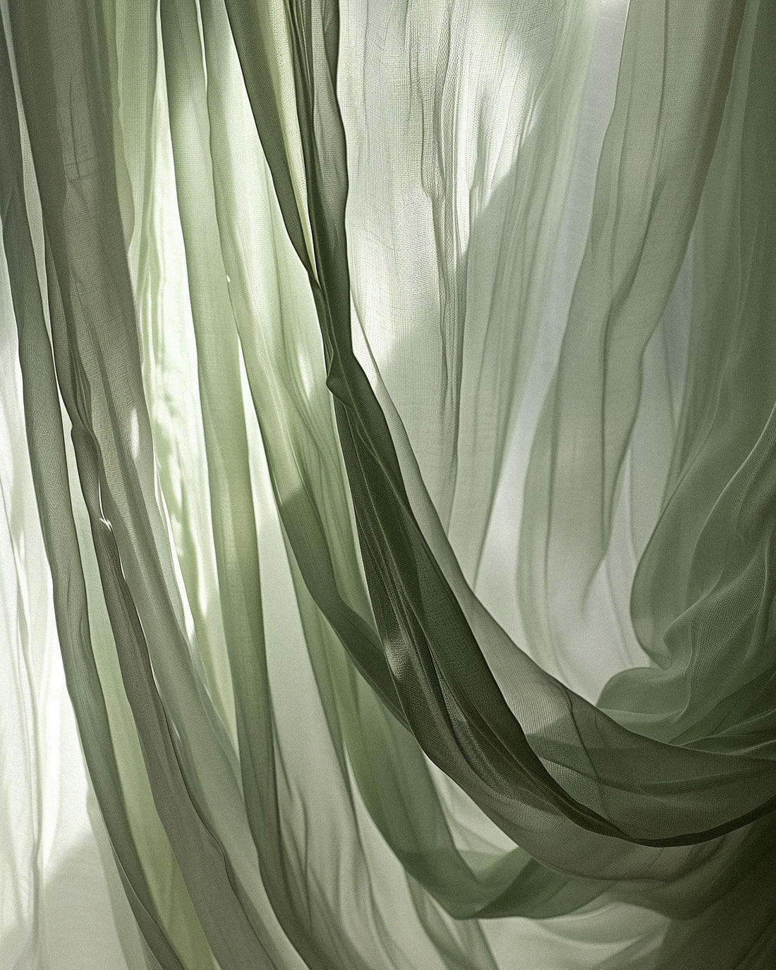A transparent, fine mesh, sage coloured draped curtain with light coming through. 