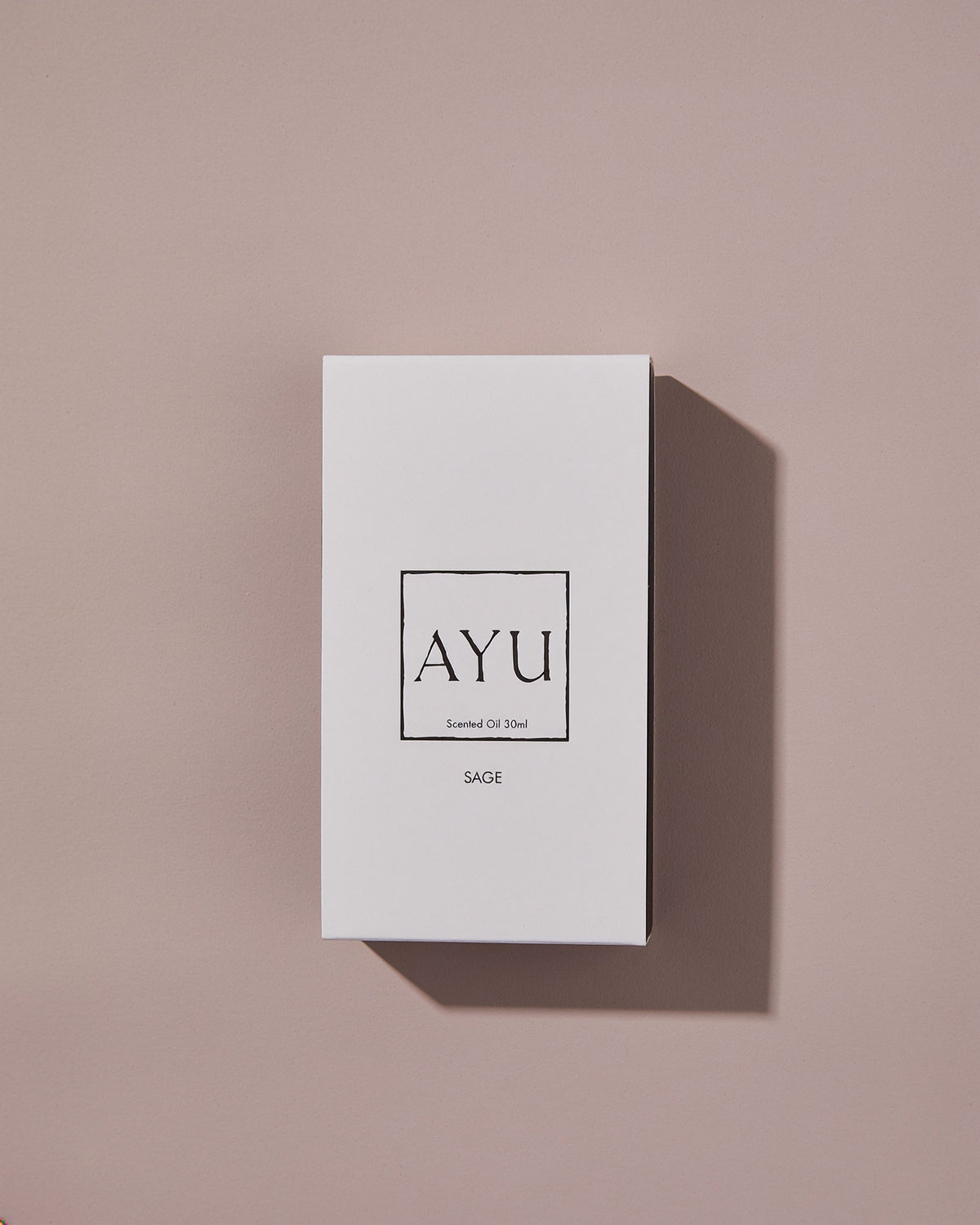 A rectangular white AYU SAGE perfume box on a dusty pink background.