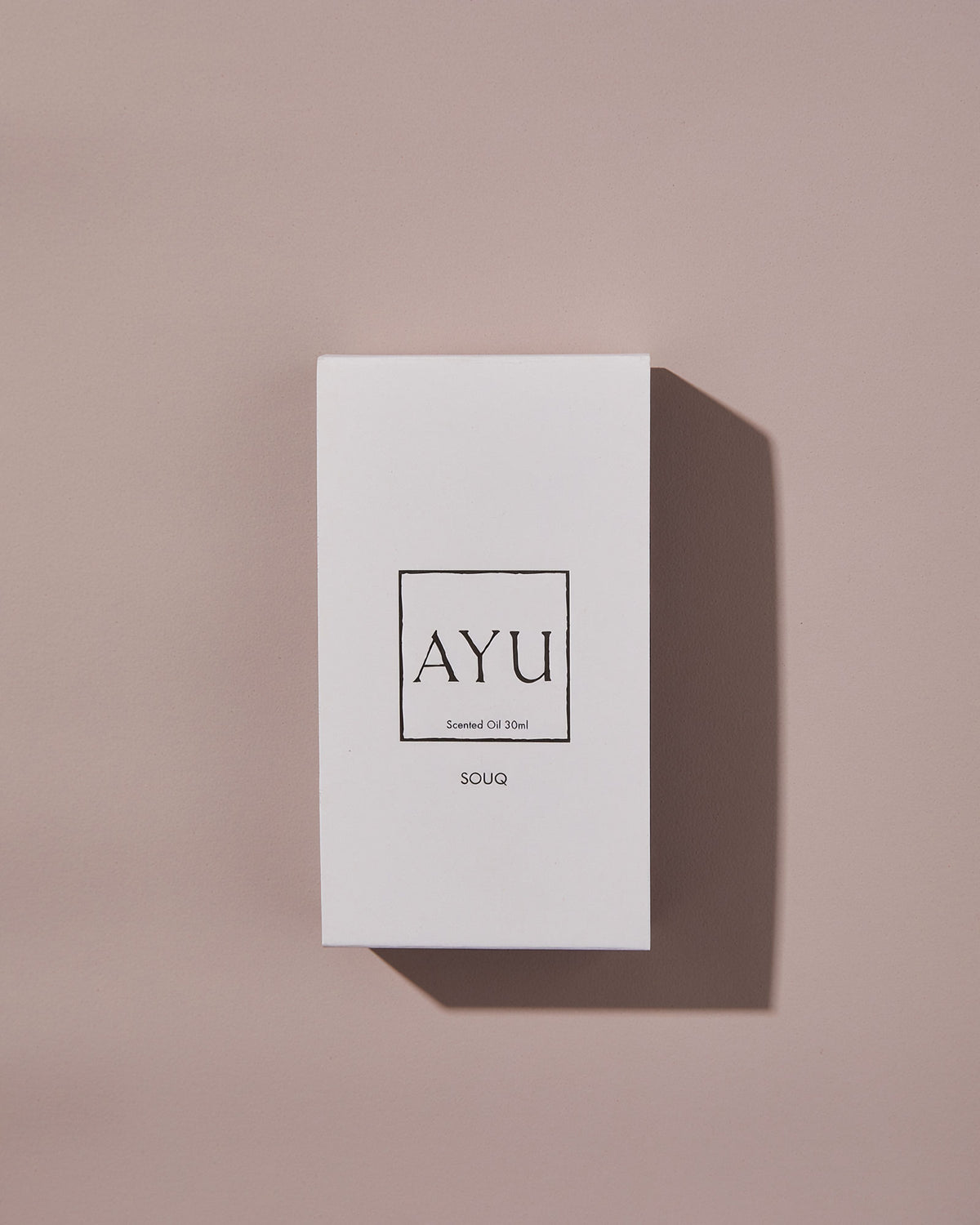 A rectangular white AYU SOUQ perfume box on a dusty pink background.