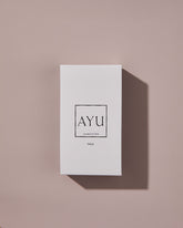 A rectangular white AYU VALA perfume box on a dusty pink background.