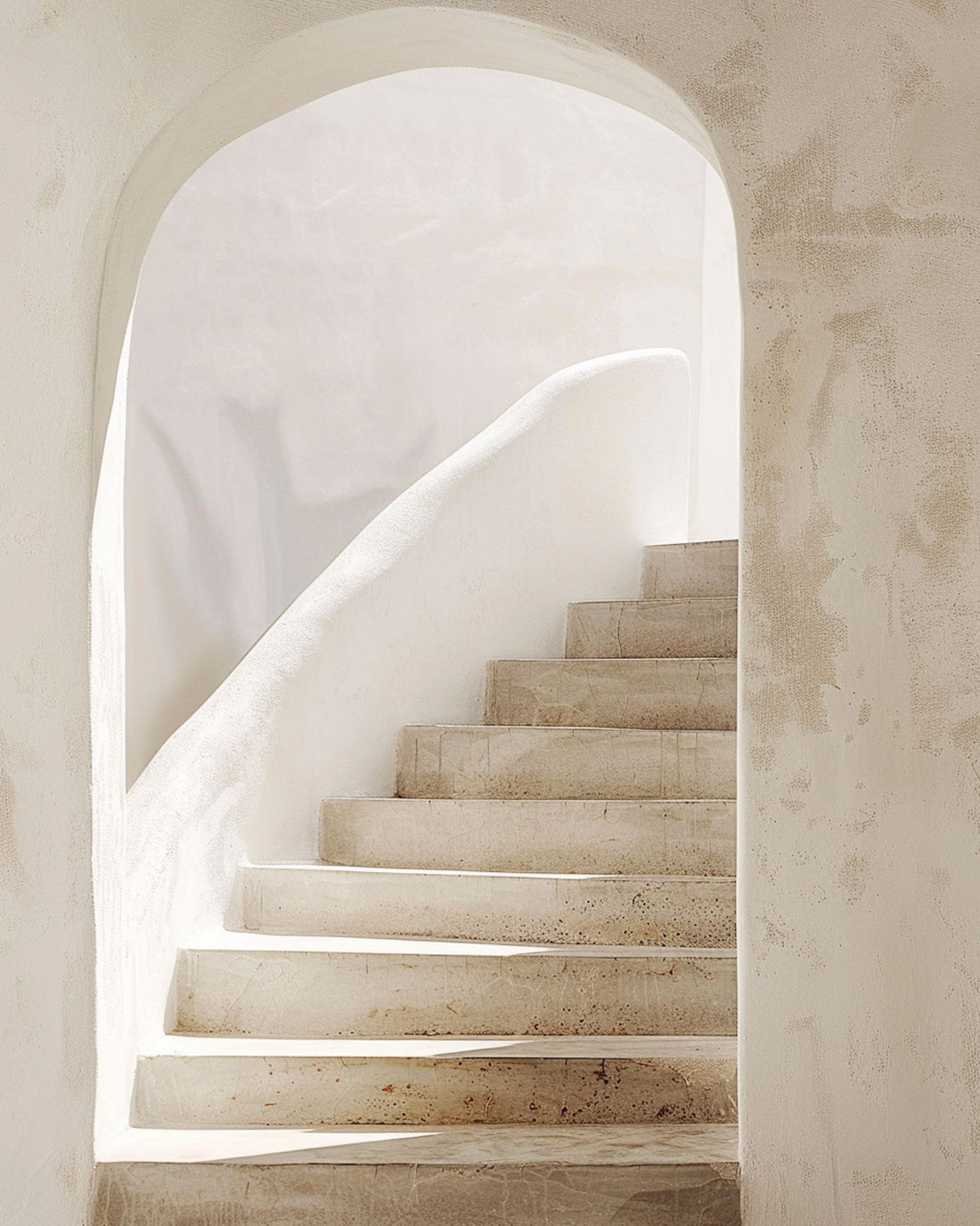 A beige textured arch leading onto a stone coloured staircase with an organic shaped, white banister and white wall. 