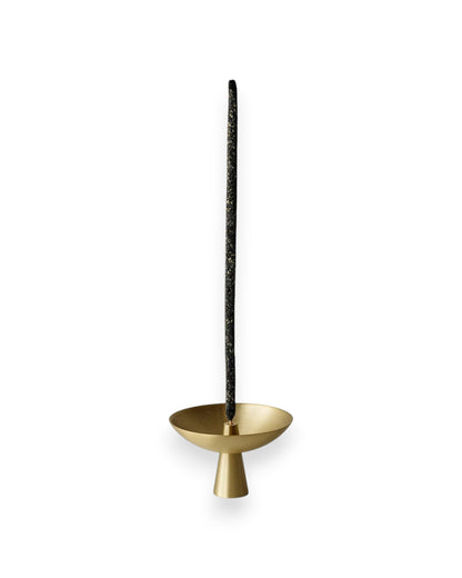 Small brass satellite shaped incense holder with a tall black incense stick standing straight up from the centre. Set against solid white background. 