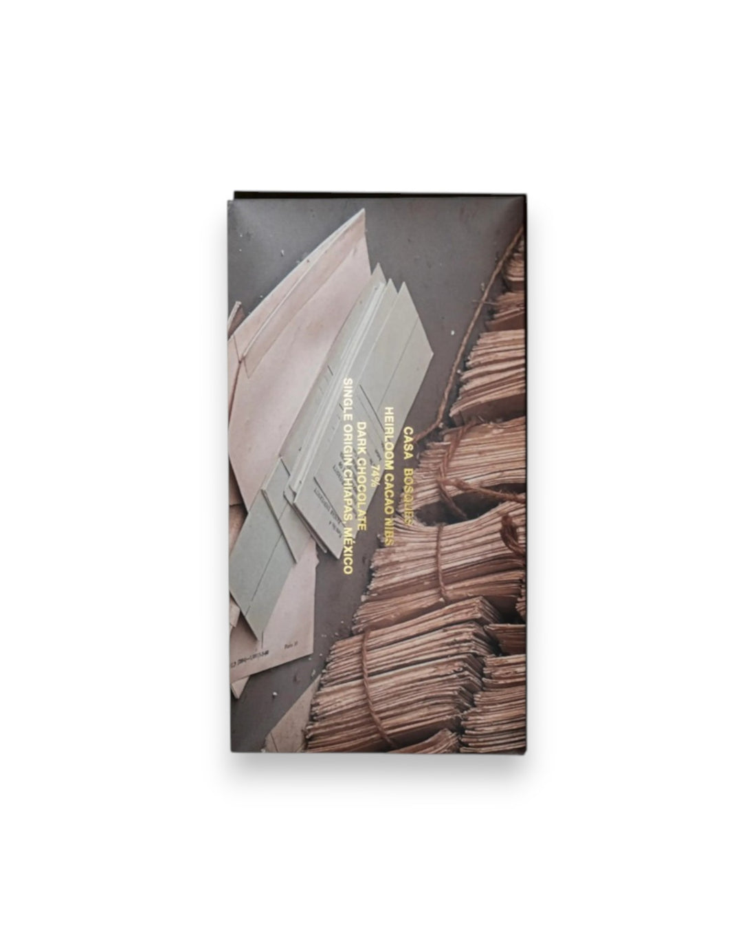 A rectangular packaged bar of Casa Bosques chocolate against a solid white background, label reads "CASA BOSQUES HEIRLOOM CACAO NIBS 74%" The graphic on packaging is a full bleed photo of a scattered papers on the floor and neatly bundled papers in the background.