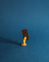 A gold ornamental hand holds a single Casa Bosques chocolate domino piece against a royal blue background. 