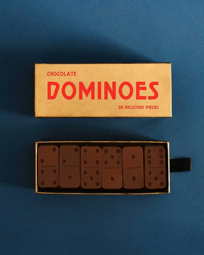 A gold-coloured rectangular boxed set of Casa Bosques chocolate dominoes is displayed with the lid off. The open box shows six chocolate domino pieces. The lid reads "CHOCOLATE DOMINOES 28 DELICIOUS PIECES"