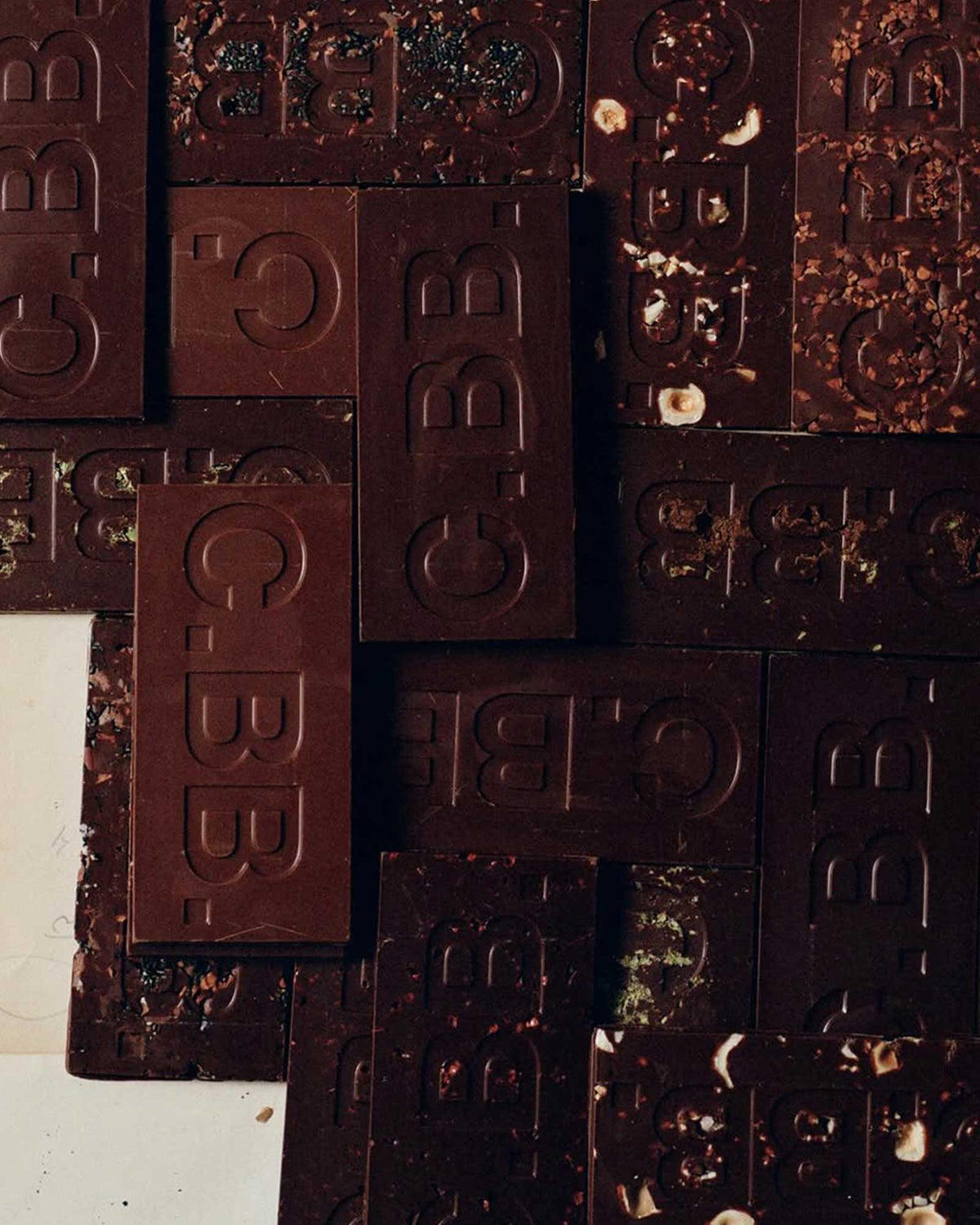 A collection of various Casa Bosques chocolate bars with no packaging. Each bar is embossed with C.BB. Bars are stacked on top of each other in a grid-like pattern.