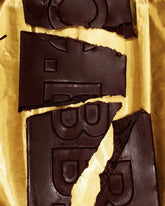 Broken pieces of a rectangular Casa Bosques dark chocolate bar showing a dark cream centre, sitting on a sheet on gold foil. 