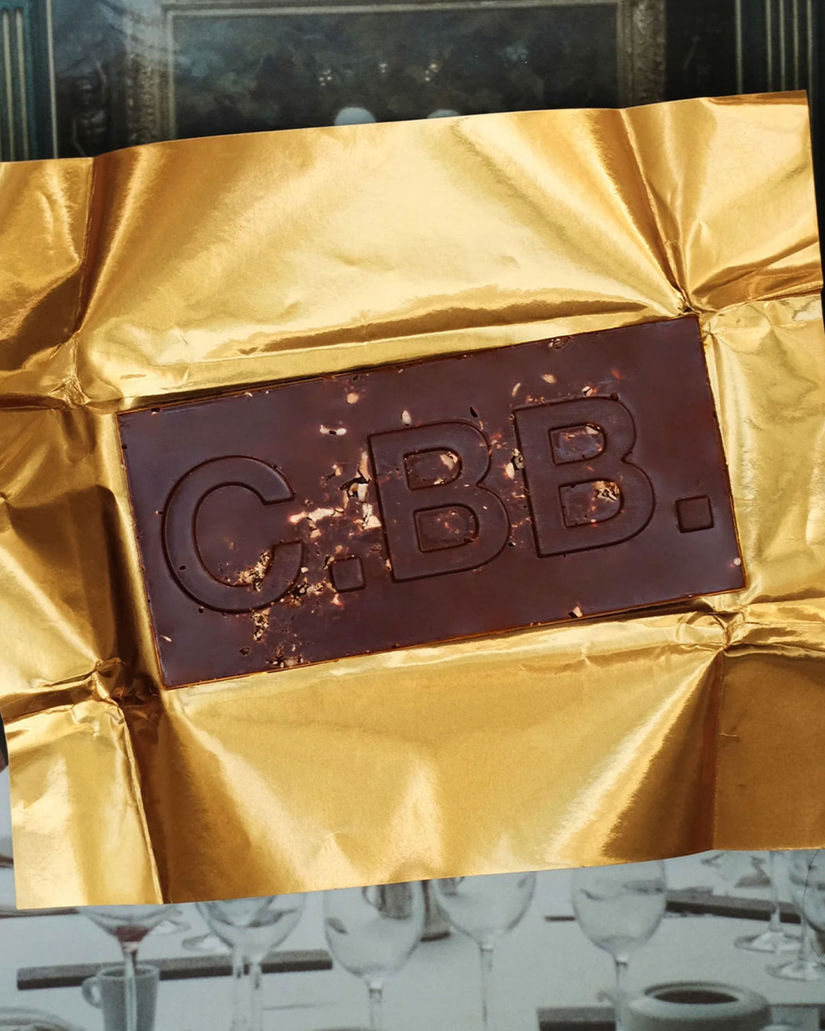 A Casa Bosques dark chocolate bar opened with C.BB. embossed on the front, bar rests on a sheet of gold foil. 