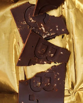 Broken pieces of a Casa Bosques dark chocolate bar sitting on a sheet on gold foil. 