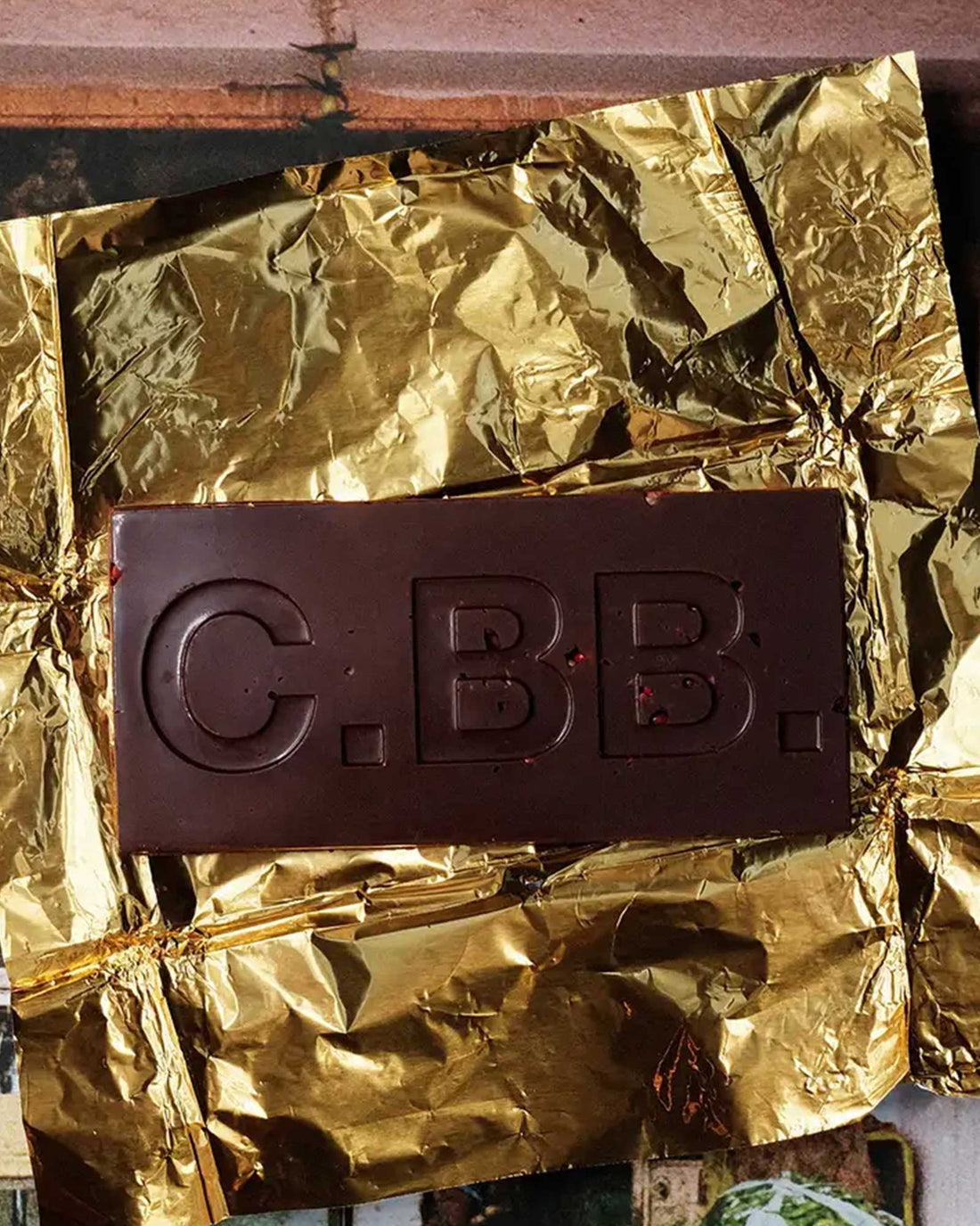 A Casa Bosques dark chocolate bar opened with C.BB. embossed on the front, bar rests on a sheet of gold foil. 