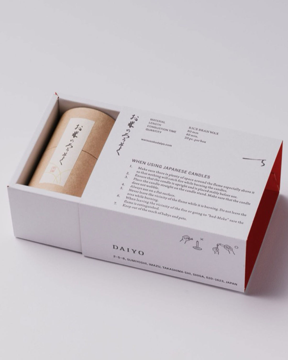 A white product box with Japanese characters and candle burning instructions printed in black ink. Box is opened slightly to reveal a cardboard canister sealed with a white label picturing Japanese characters. 
