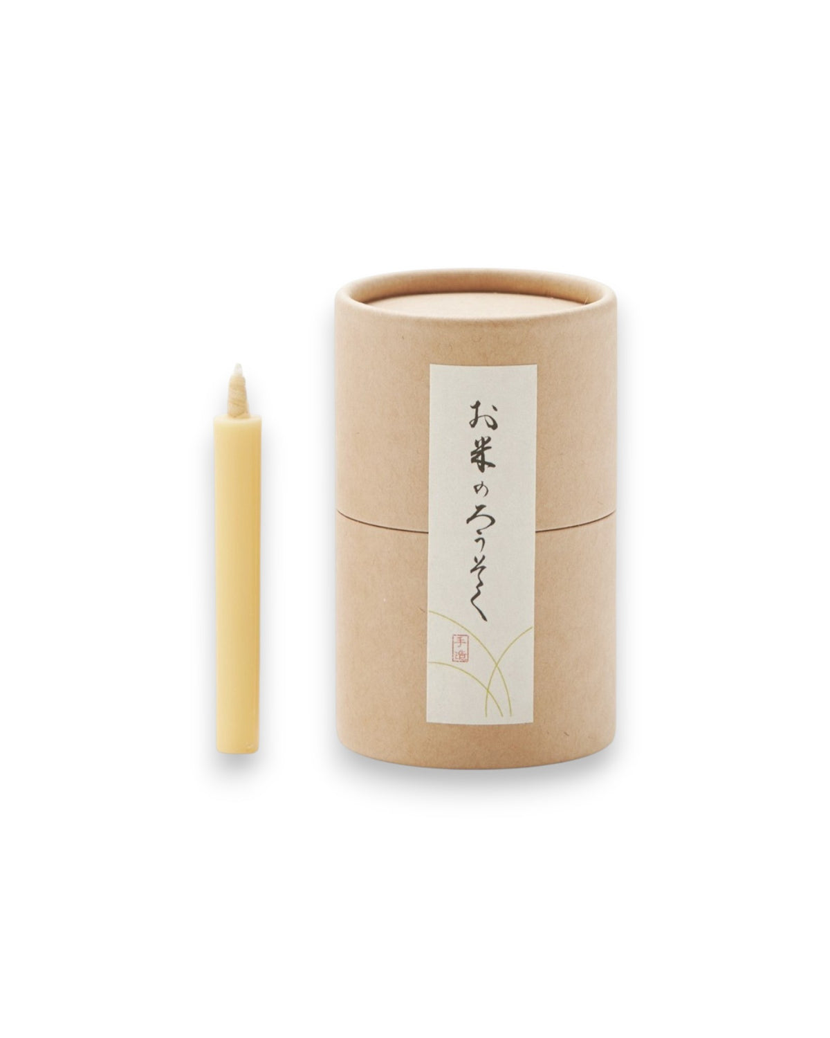 Product shot of one natural-coloured tapered candle alongside a cardboard canister, sealed with a label picturing Japanese characters. 