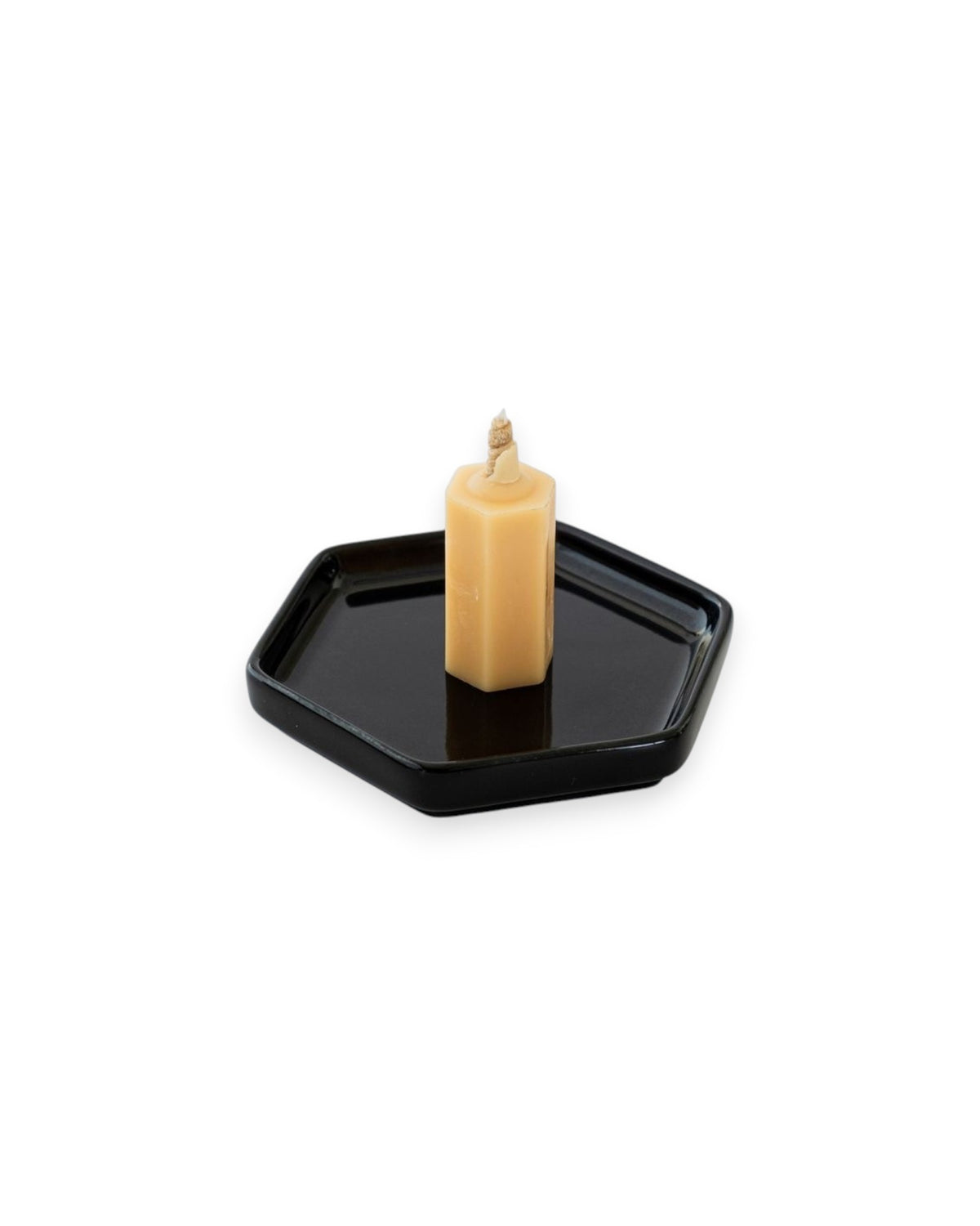 A small honey coloured candle sits on a black hexagon shaped plate on a solid white background. 