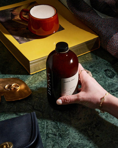 A hand holds a dark amber bottle of Dona&