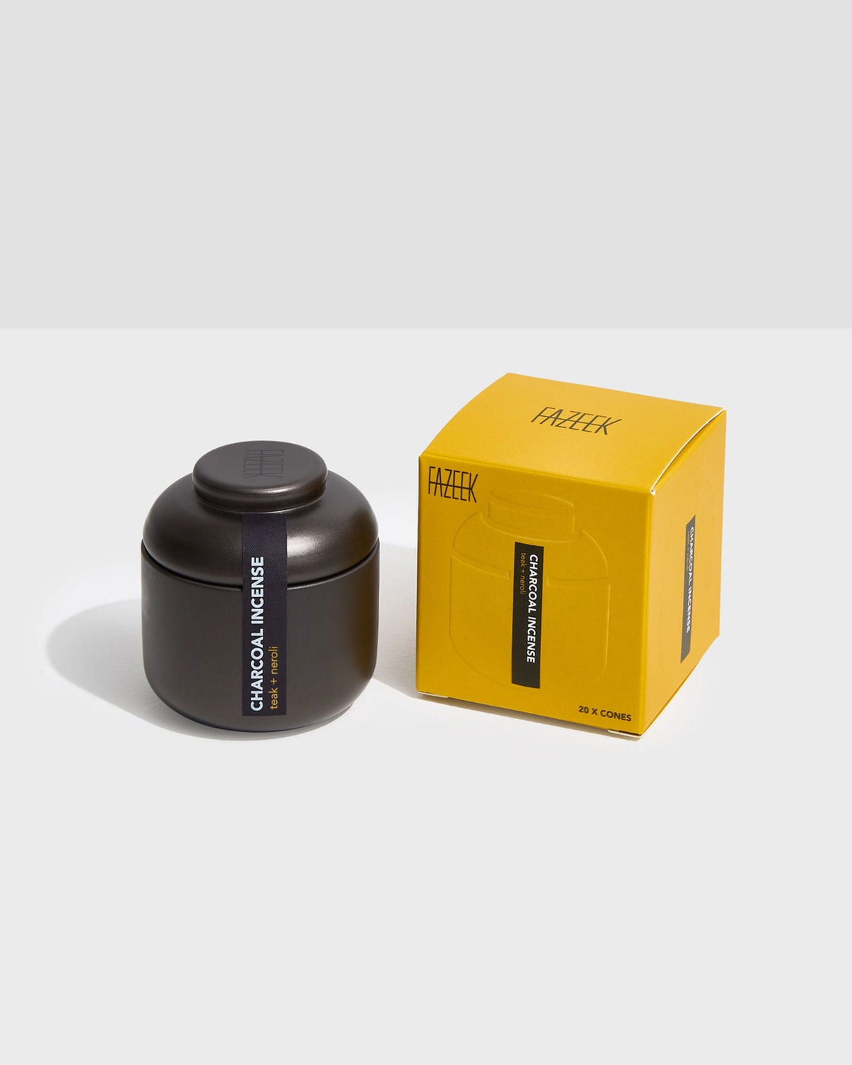 Product shot showing a charcoal-coloured tin canister alongside its cardboard box packaging. Both the tin canister and light yellow box are labelled "CHARCOAL INCENSE teak and neroli".