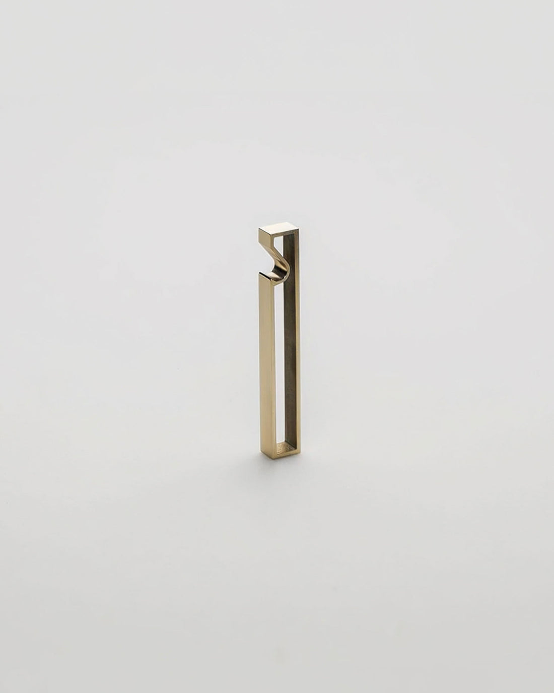 A minimalist, modern geometric bottle opener with a gold brushed metal finish, standing upright on a seamless light grey background.