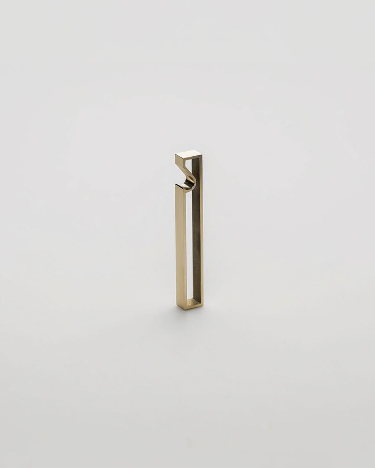 A minimalist, modern geometric bottle opener with a gold brushed metal finish, standing upright on a seamless light grey background.