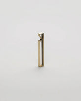 A minimalist, modern geometric bottle opener with a gold brushed metal finish, standing upright on a seamless light grey background.