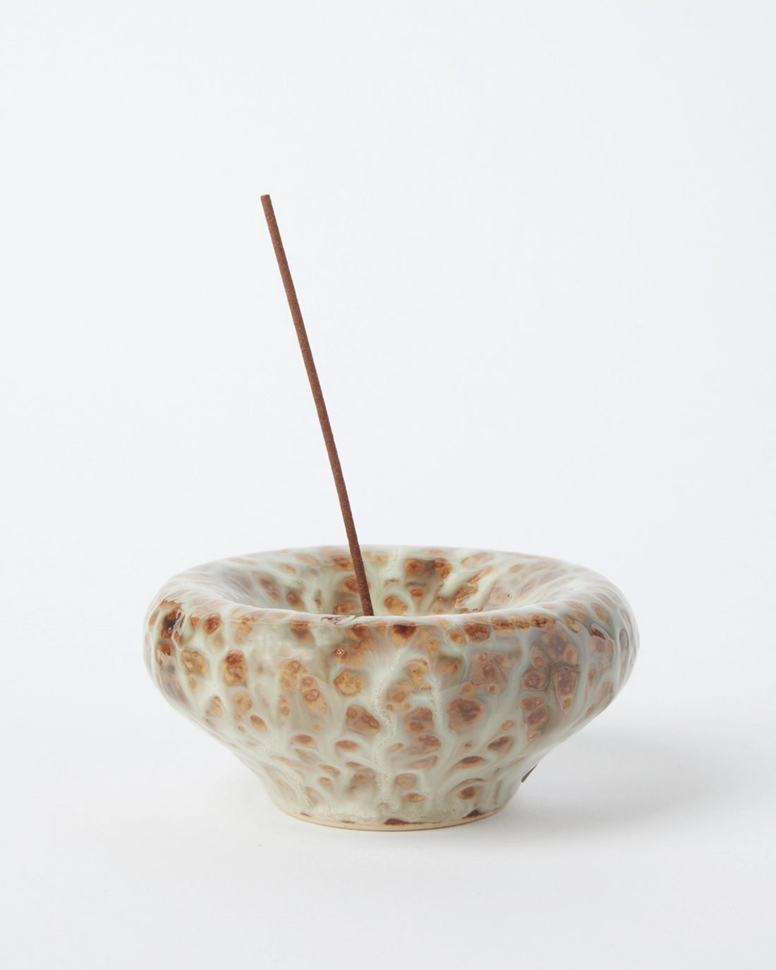 A textured ceramic incense holder with a brown incense stick inserted, set against a clean white background.