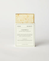 Herb Remedy Calendula botanical soap bar in a white paper sleeve packaging, showing the textured off-white soap bar with small specks at the top, on a clean white background.