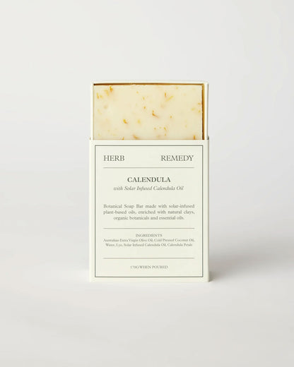 Herb Remedy Calendula botanical soap bar in a white paper sleeve packaging, showing the textured off-white soap bar with small specks at the top, on a clean white background.