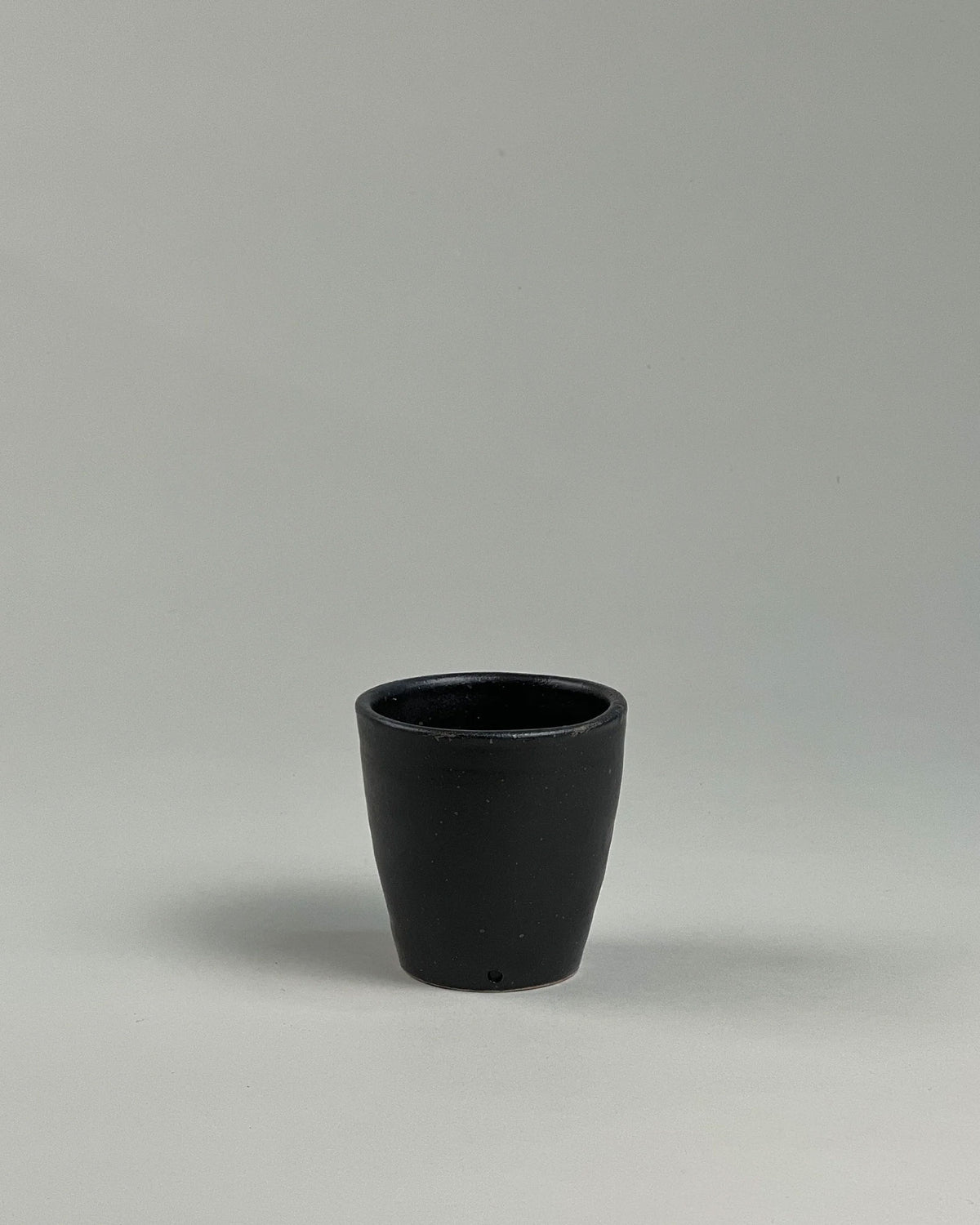 A short black ceramic drinking tumbler on a seamless, light grey background. 
