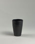 A tall black ceramic drinking tumbler on a seamless, light grey background. 