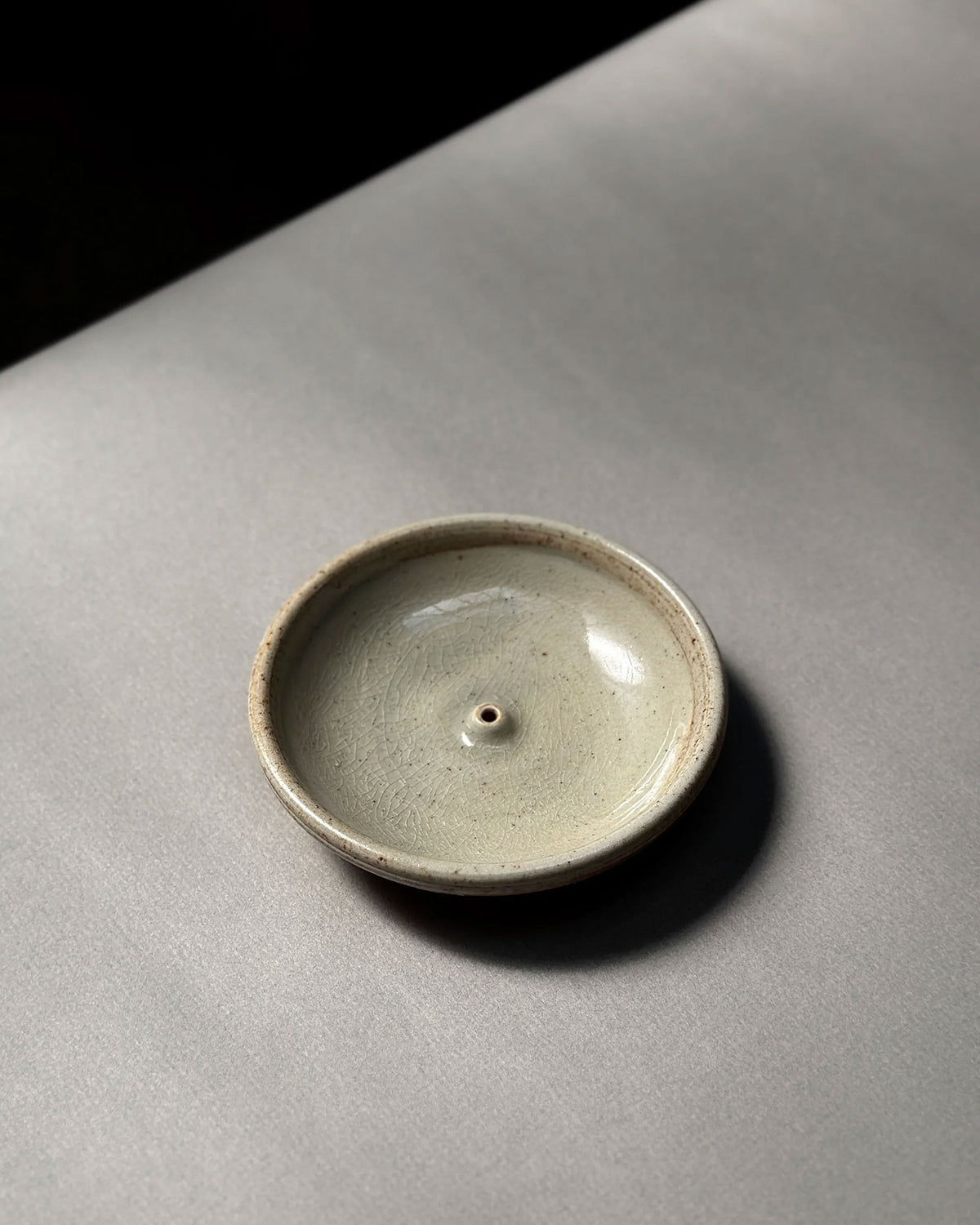 A natural-coloured, round, bowl-like, ceramic incense holder sits on a light grey table surface.
