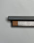 A long, rectangular, grey box is open to show a wrapped bundle of light brown incense sticks, the lid of the same colour sits above the incense. On the side of the lid in light blue printed lettering, it reads Made in Tibet, White sandalwood, Red Sandalwood, Saffron Crocus, Safflower, Berley Wine, Palo Santo. Set on a seamless light grey background. 
