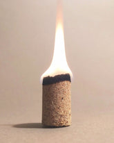 An Incausa Palo Santo Incense Briquette with a bright white and yellow flame, standing upright on a neutral beige background.
