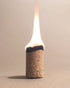 An Incausa Palo Santo Incense Briquette with a bright white and yellow flame, standing upright on a neutral beige background.