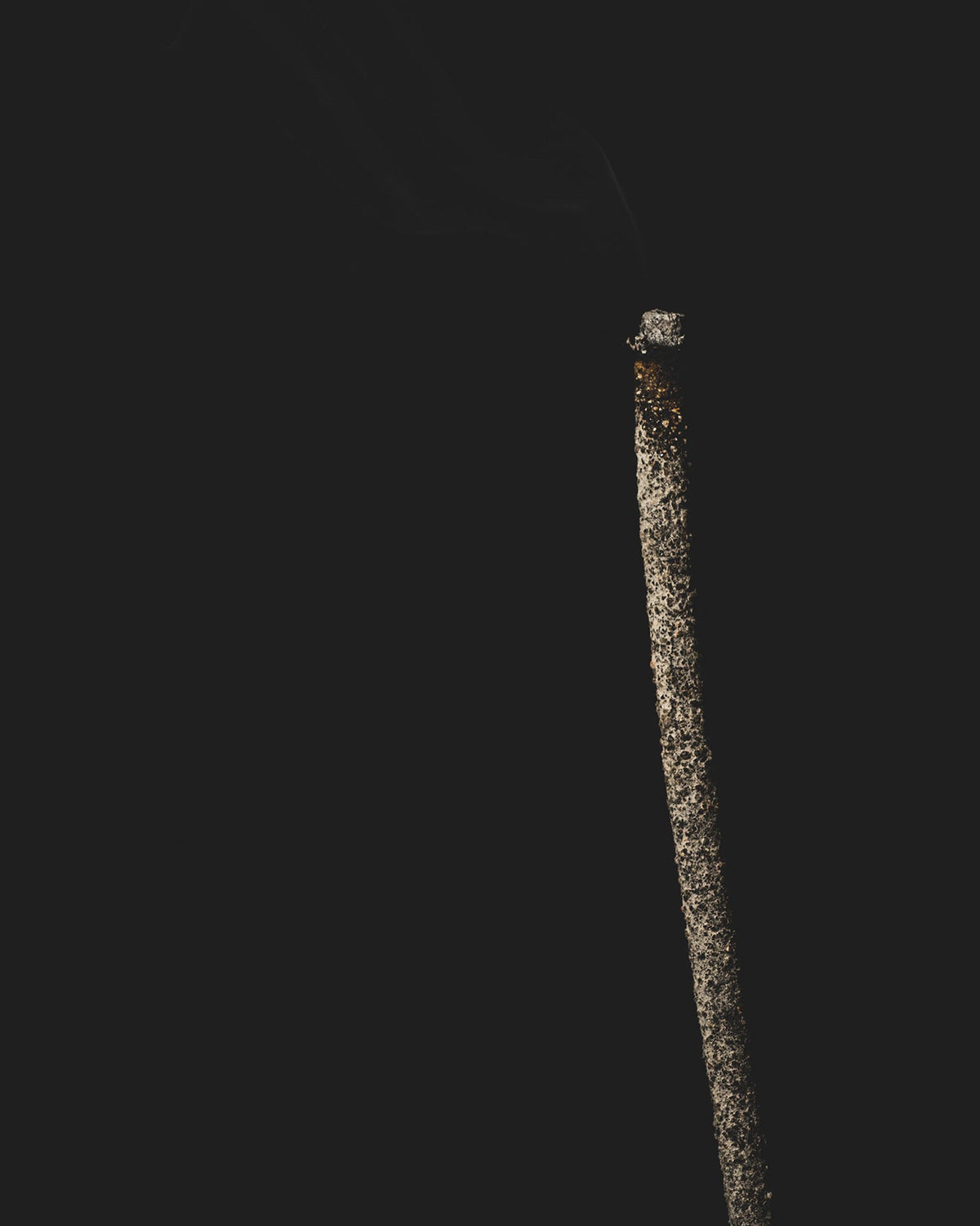 A tall dark incense stick is smouldering against a black background.