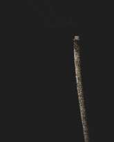 A tall dark incense stick is smouldering against a black background.