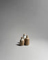 A grouped set of three ceramic bottles with cork lids and a rustic white and brown glaze on a seamless, light grey background. 
