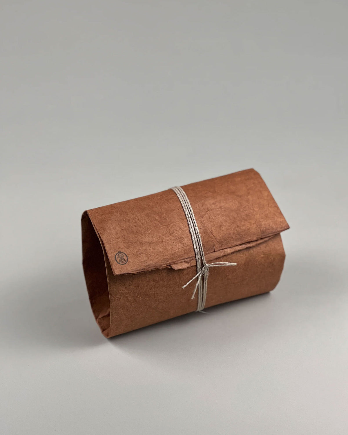 A brown paper and string wrapped rectangular parcel on a seamless, grey background. 
